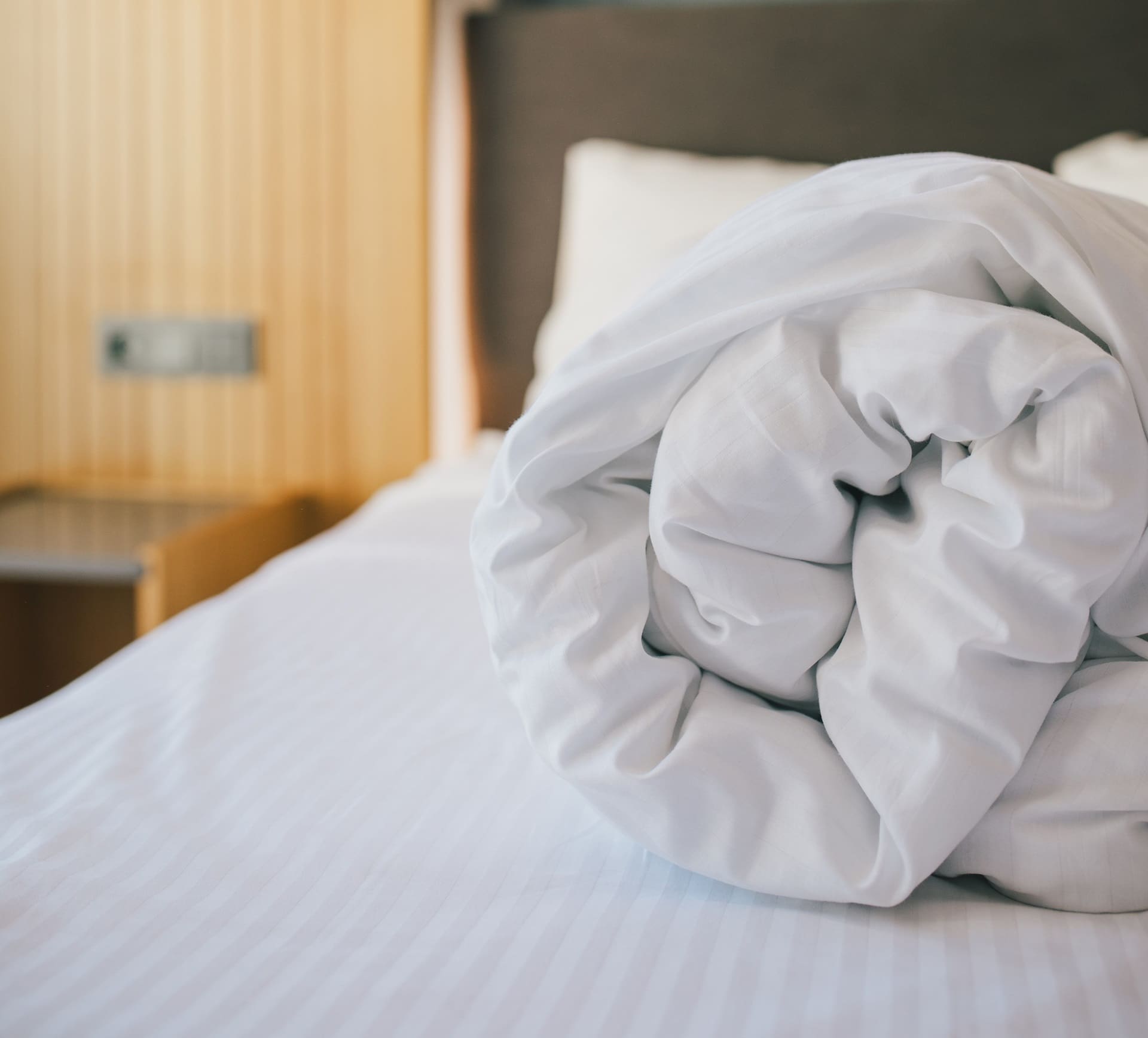 Rolled white comforter on a neatly made bed, emphasizing cleanliness and comfort for professional bedding services.